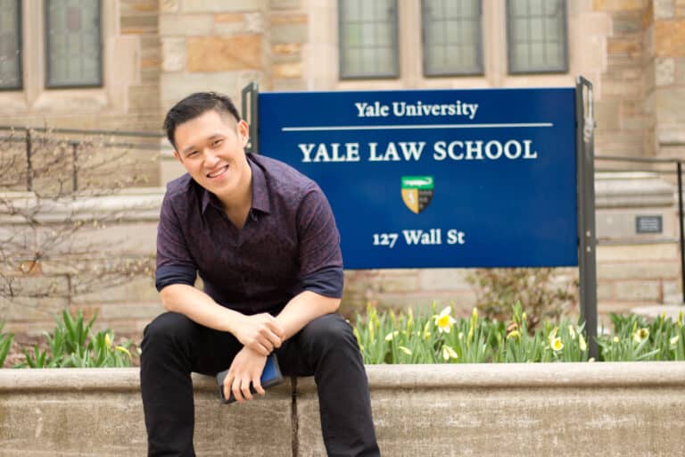 Ryan Liu sits next to a sign
